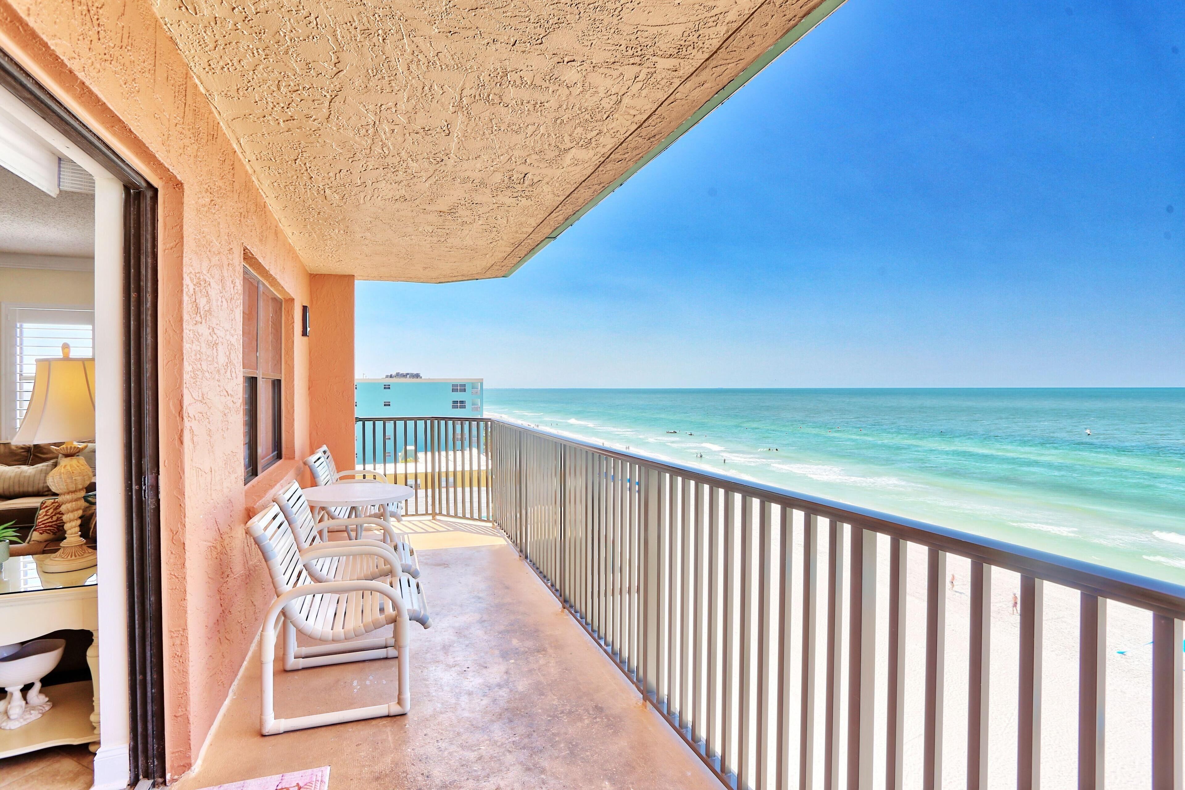 Ein Balkon mit Blick auf den Strand, einem Tisch mit Stühlen und einem Geländer.