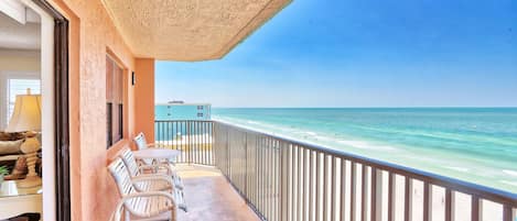 A balcony with a view of the beach, a table with chairs, and a railing.