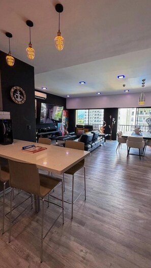A modern living room with a dining area, a flat-screen TV, and a large window with a city view.