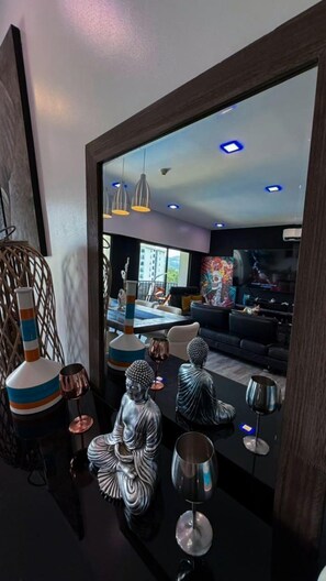 Un interior moderno con comedor, un espejo grande que refleja la habitación y estatuas decorativas.