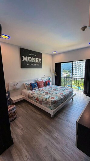 Une chambre avec un grand lit, une vue sur un immeuble et un plafond doté d’un éclairage encastré.