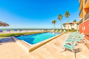 A swimming pool with lounge chairs, a palm tree, and a view of the ocean.
