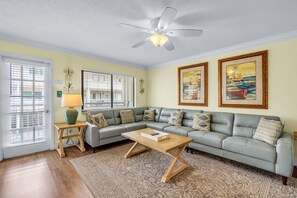 A living room with a grey sofa, a wooden coffee table, a ceiling fan, and two framed paintings.