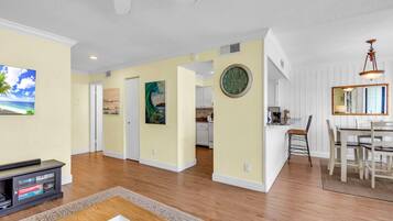 A spacious living area with a dining table, kitchen, and a large clock on the wall.