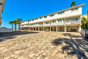 A multi-story hotel with a covered outdoor area, palm trees, and a clear blue sky. - Gulfside Villas 3 (Indian Rocks Beach)