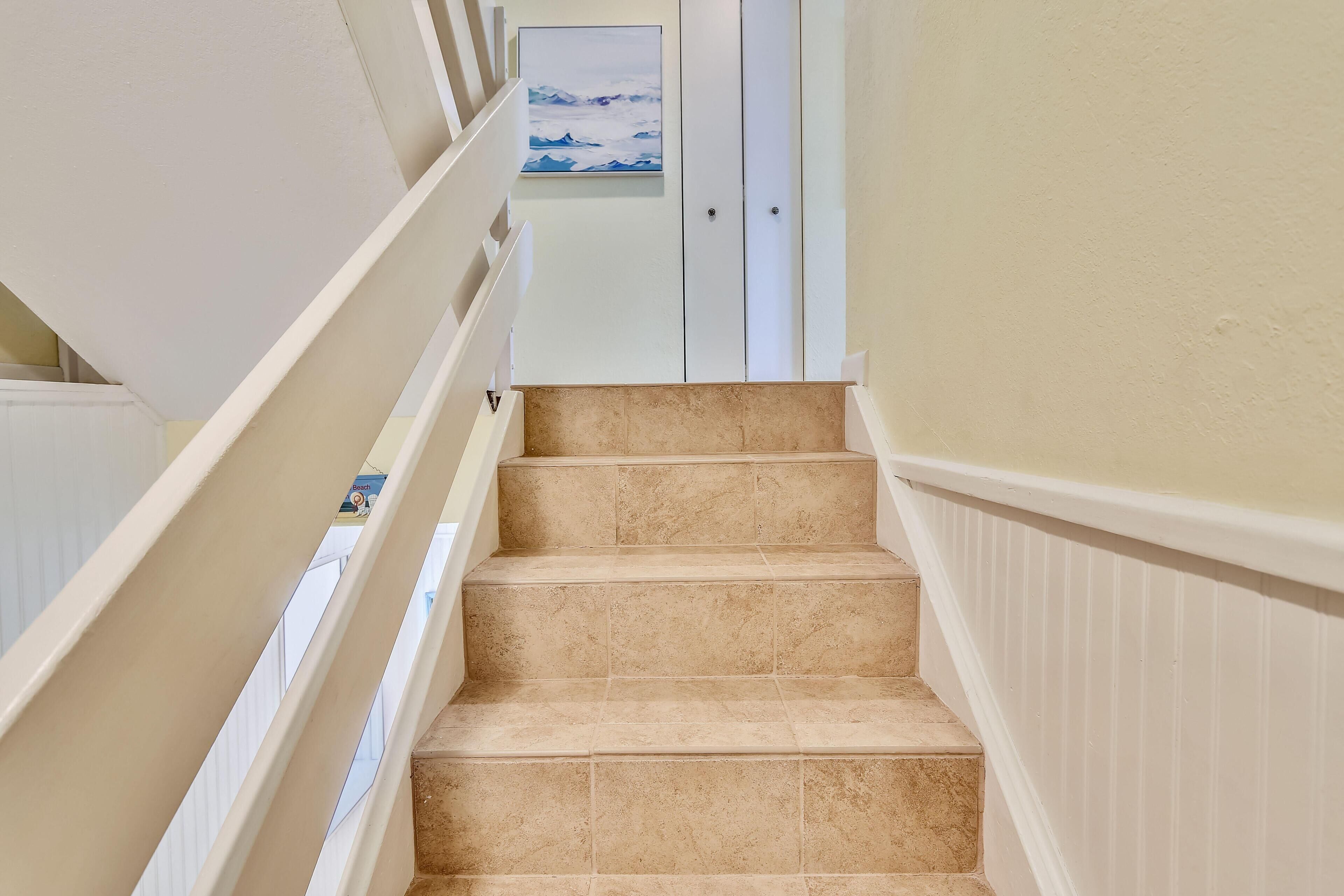 A staircase with beige tiles and white railings leading to a door with a painting above it.
