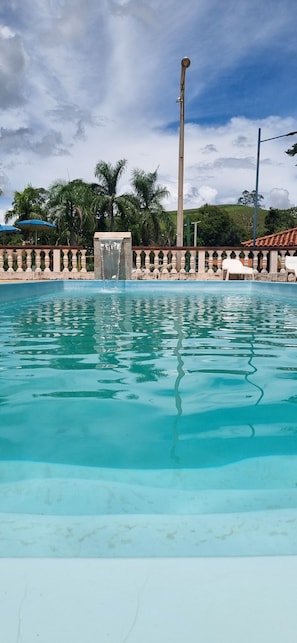 A swimming pool with a water feature, surrounded by a balustrade and palm trees.