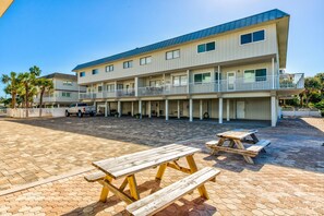 A multi-story hotel with a covered outdoor area, picnic tables, and a parking lot.
