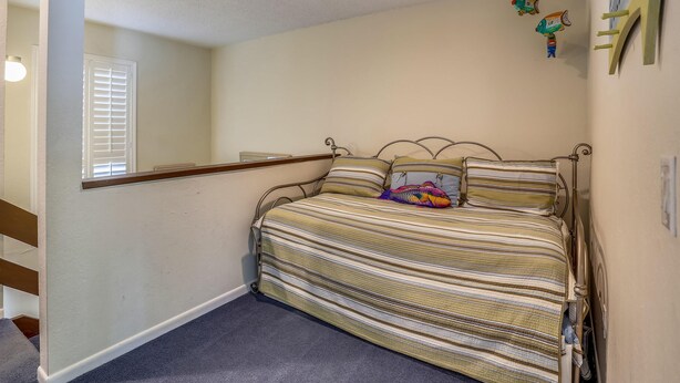 Un dormitorio con cama, ventana con persianas, estante montado en la pared y un pequeño adorno en la pared.