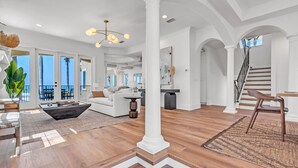 A spacious living area with a large white column, a staircase, and a view of the outdoors.