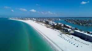 A coastal cityscape with a wide beach, clear blue waters, and a mix of residential and commercial buildings.