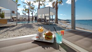 A beachside dining area with a view of the ocean, a pool, and palm trees. - The Palms Resort - Villa President Beach I (Tkon)