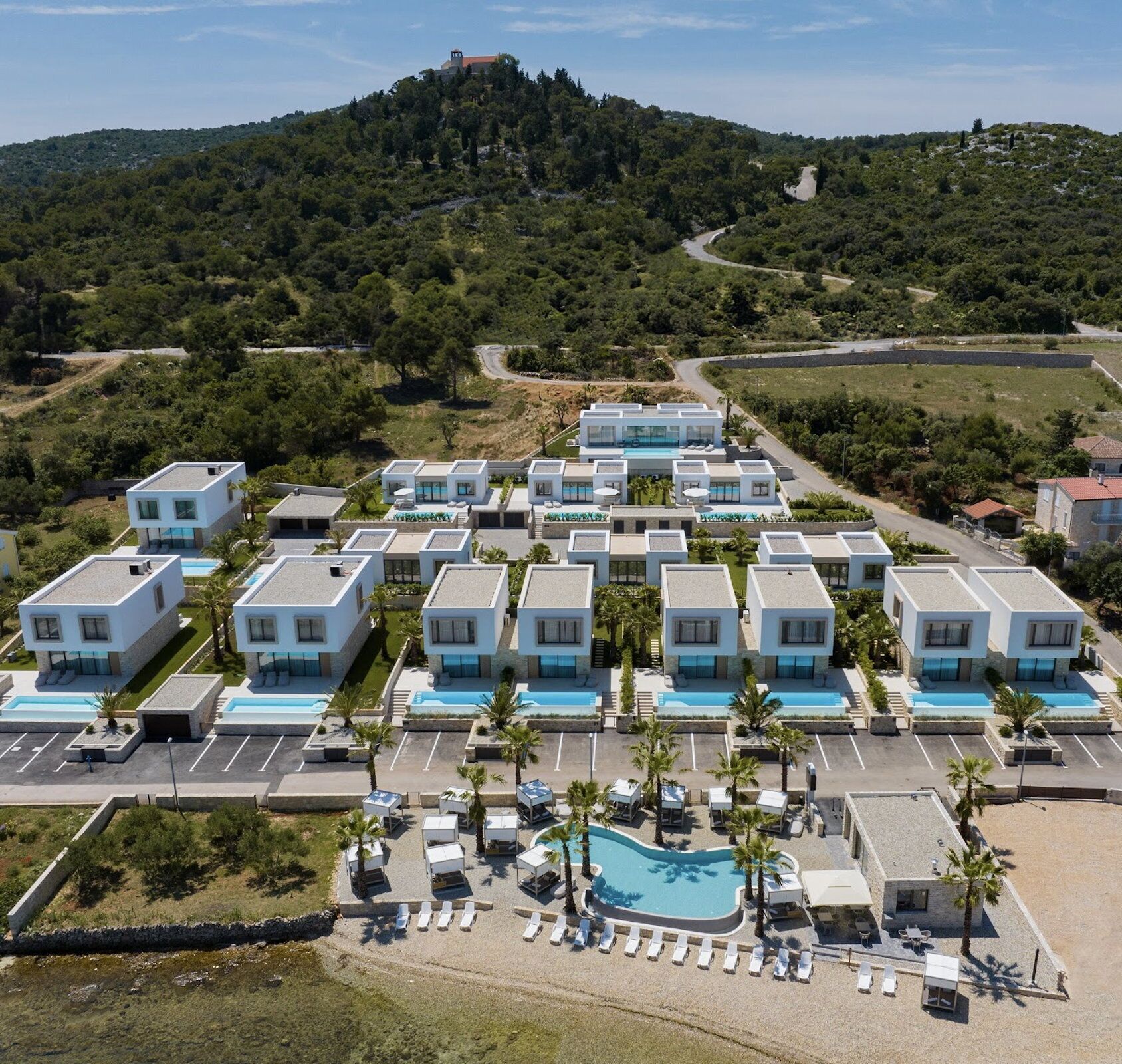 Un moderno complejo turístico con varias construcciones, una piscina y un paisaje montañoso de fondo.