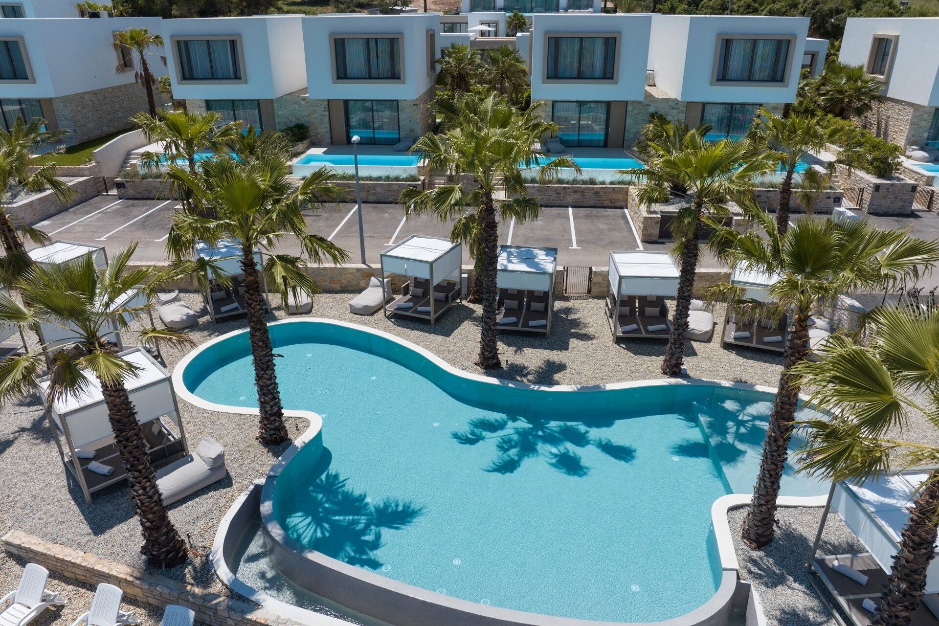 Un hôtel moderne doté d’une piscine centrale, entourée de palmiers et de chaises longues.