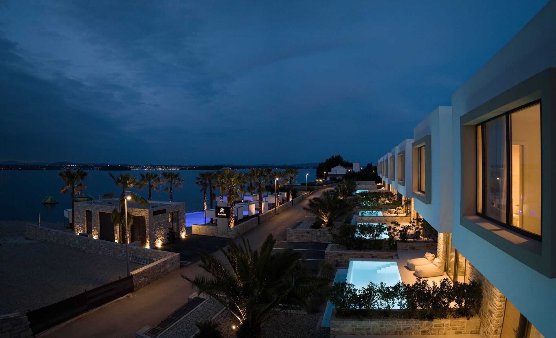 Ein modernes Hotel mit Pool, Palmen und Meerblick bei Nacht.