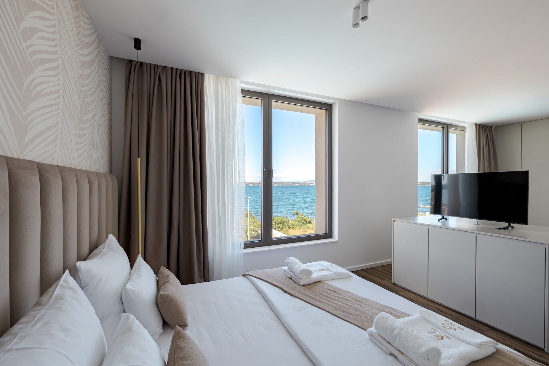 Habitación de hotel moderna con una cama grande, un televisor y vista al mar.