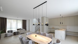 Una sala de estar moderna con una mesa de comedor de mármol, sillas tapizadas en gris, un sofá y una escalera con barandales negros.