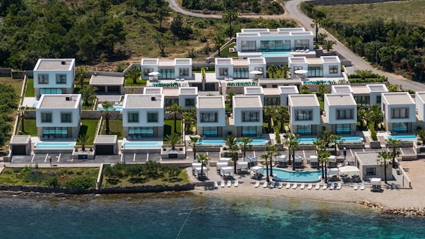 Un moderno resort con varias construcciones, un área de piscina y acceso directo a la playa.