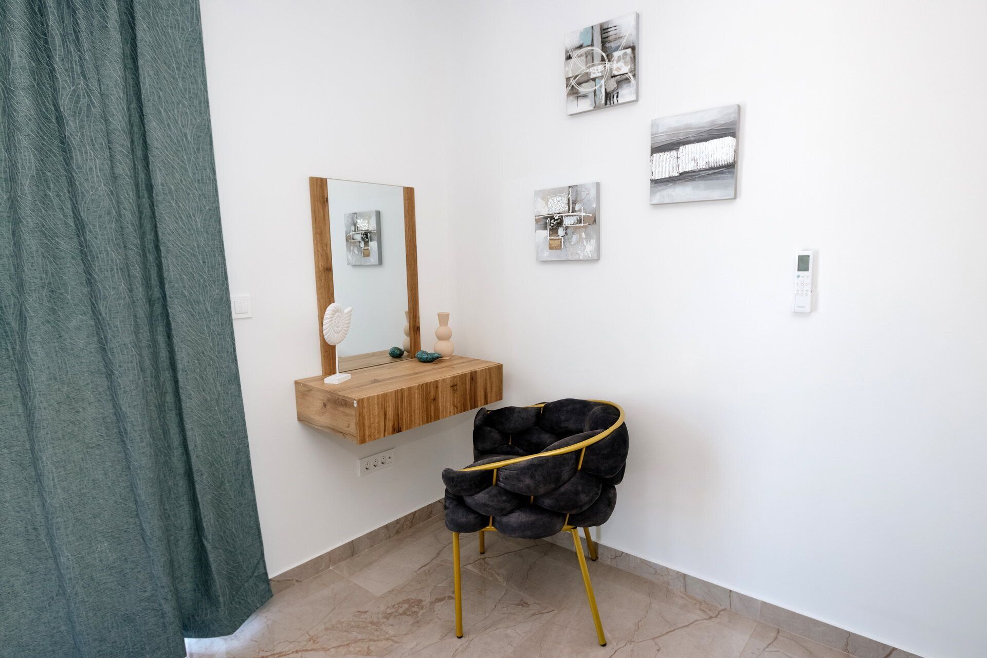 A bathroom with a wooden vanity, a mirror, a black chair, and three abstract wall art pieces.