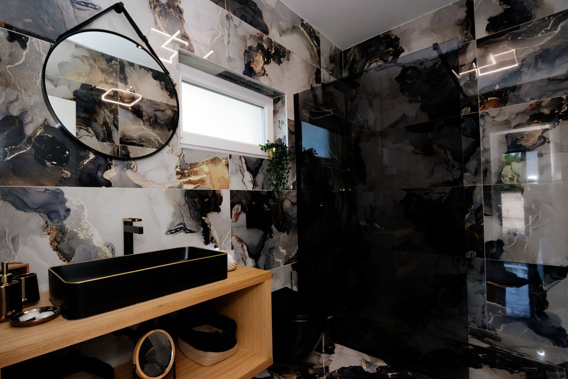 Une salle de bain moderne avec un lavabo noir, des murs en marbre et un miroir rond.
