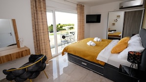 A modern hotel room with a bed, a TV, a balcony with a table and chairs, and a mirror. - Villa Emerilla with Pool (Pula)