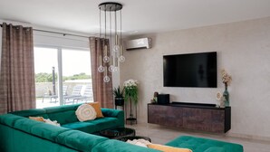 A living room with a green sofa, a flat-screen TV, and a ceiling light fixture. - Villa Emerilla with Pool (Pula)