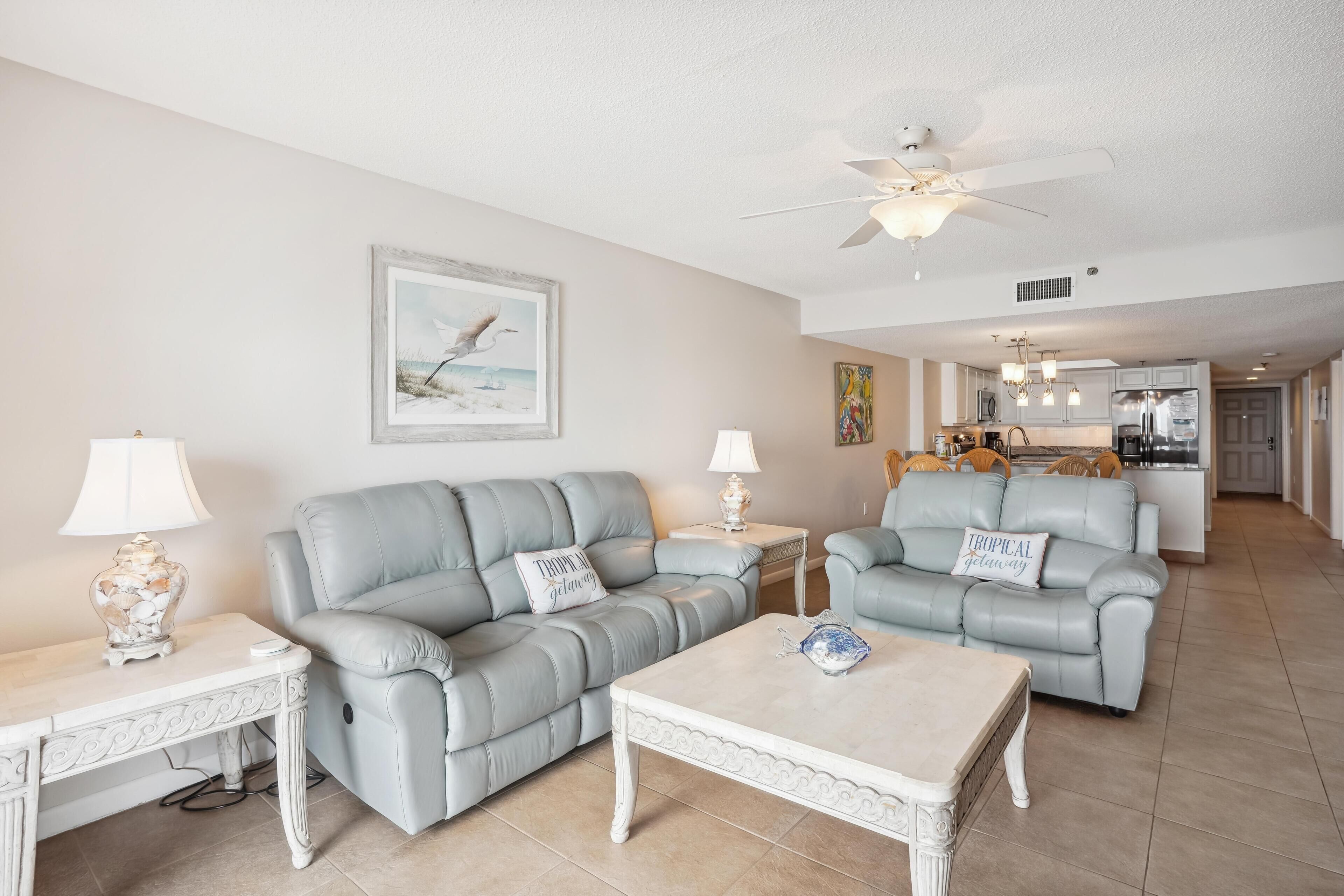 A spacious living room with two grey leather sofas, a white coffee table, and a ceiling fan.