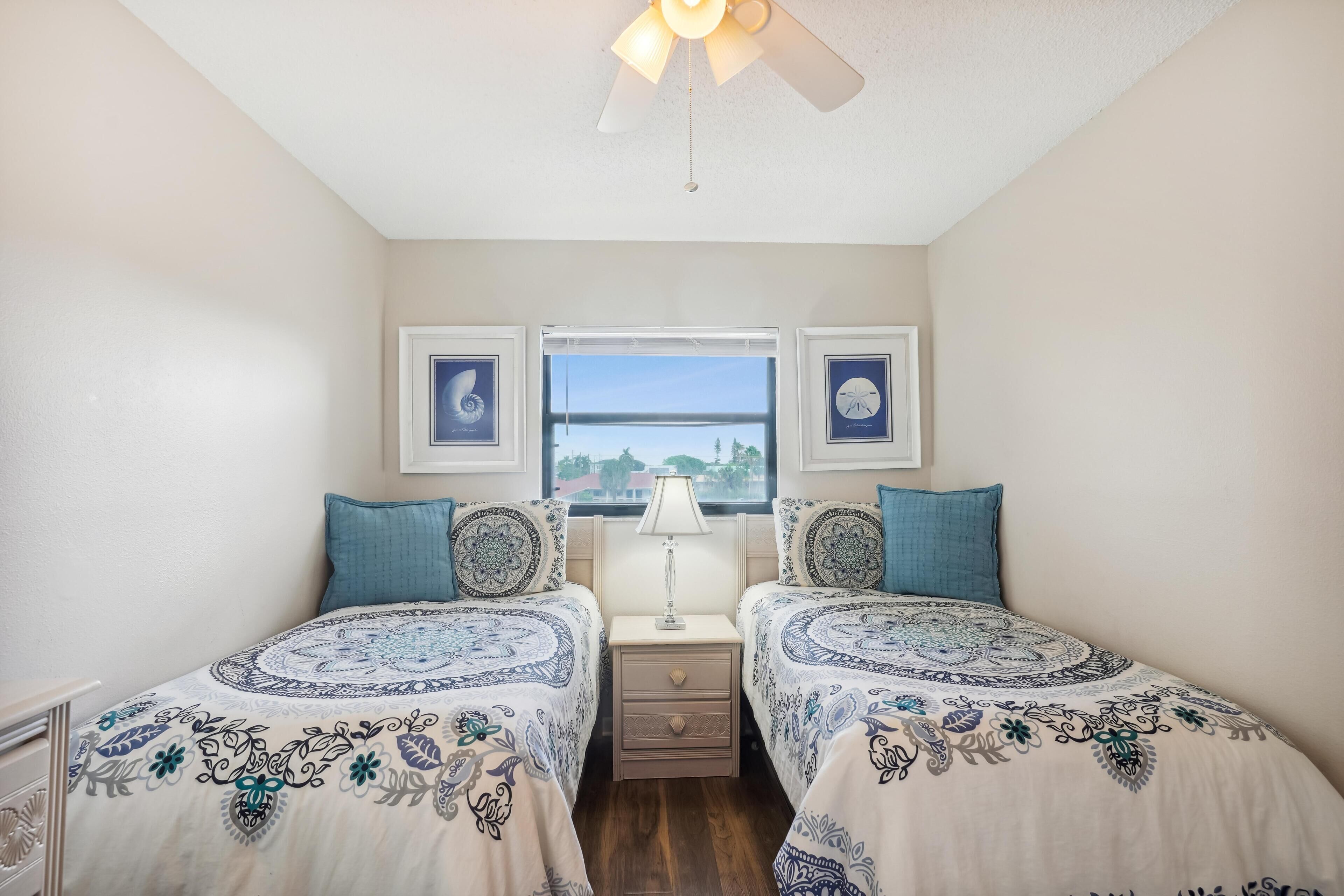 A bedroom with two beds, a window with a view, and a ceiling fan.