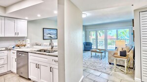 A modern kitchen with white cabinets, a dishwasher, and a large window. - Land's End 1-203 Pool View (Treasure Island)