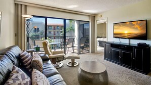 A modern living room with a leather sofa, a round coffee table, and a flat-screen TV mounted on the wall. - Land's End 1-301 Gulf View - Premier (Treasure Island)