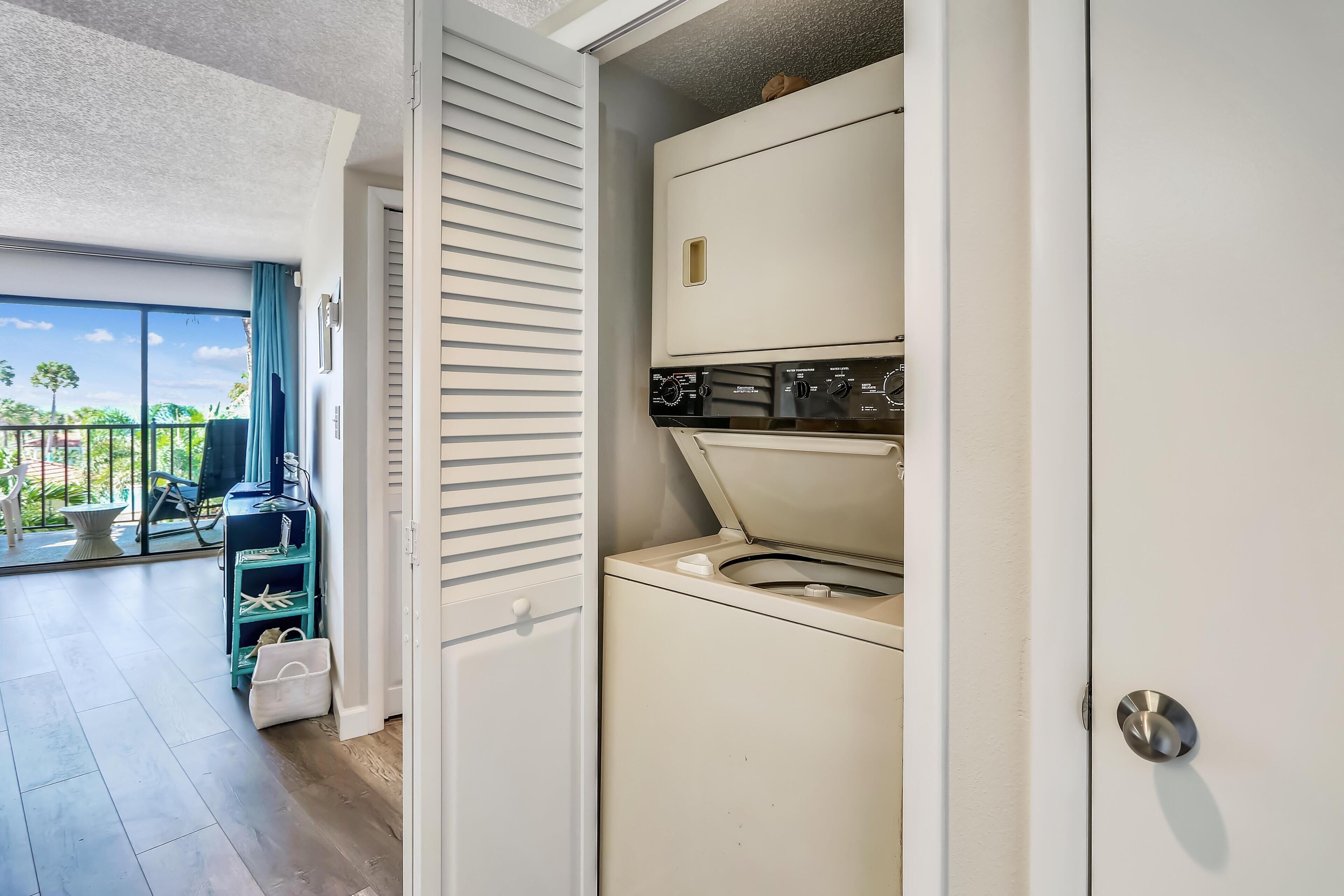 A compact laundry room with a washing machine and dryer, a sliding door, and a view of the outdoors through a glass door.