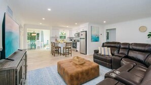 A modern living room with a leather sofa, a wooden TV stand, and a dining area with chairs and a table. - Relaxing pool, Elegant and FUN vacation home! (Clearwater)
