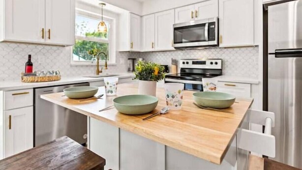 A modern kitchen with white cabinets, a wooden island, stainless steel appliances, and a view of greenery outside. - Relaxing pool, Elegant and FUN vacation home! (Clearwater)