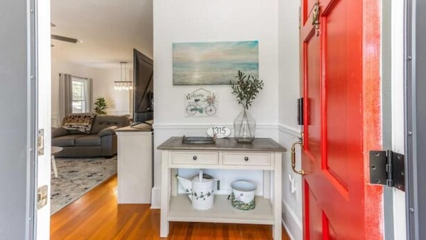 A hallway with a red door, a white console table with decorative items, and a painting on the wall.