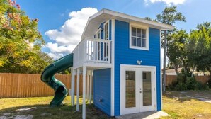 A blue and white playhouse with a slide, a door, and a small porch.