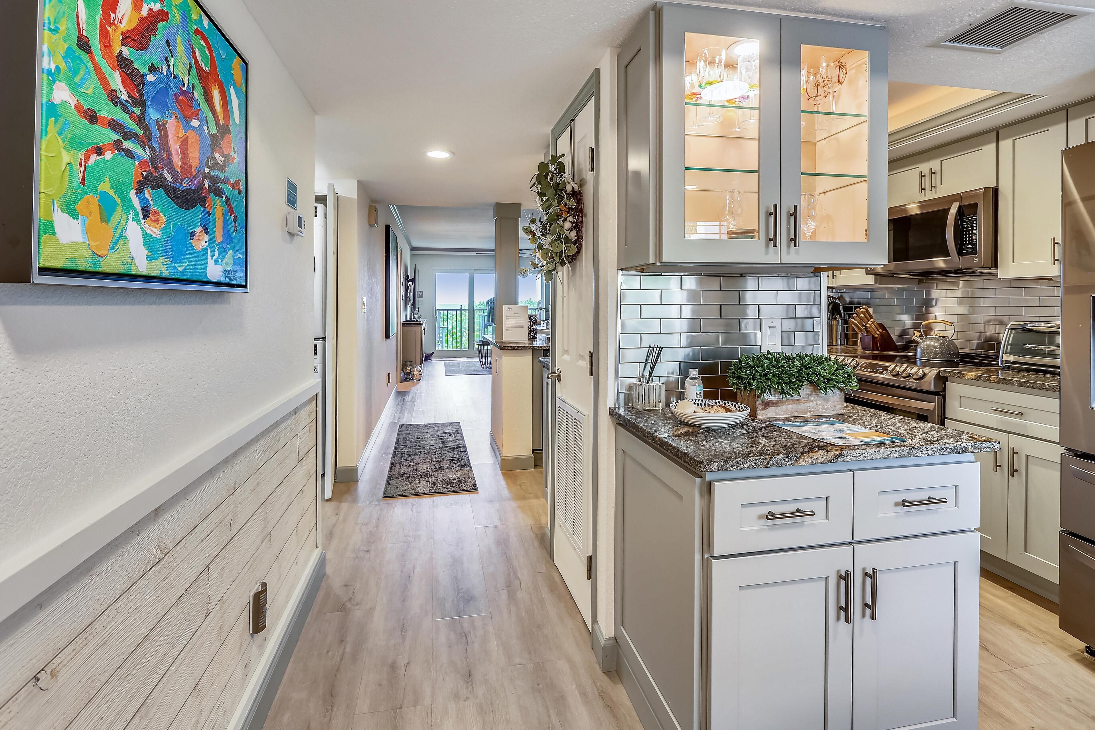 A modern kitchen with stainless steel appliances, white cabinetry, and a colorful abstract painting on the wall.