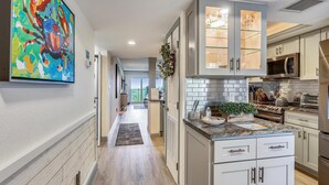 A modern kitchen with stainless steel appliances, white cabinetry, and a colorful abstract painting on the wall. - Land's End 10-202 Beach Front - Premier (Treasure Island)
