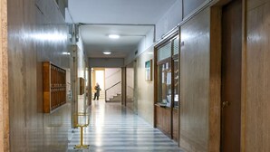 Um corredor com piso de mármore, portas de madeira e um suporte de metal.