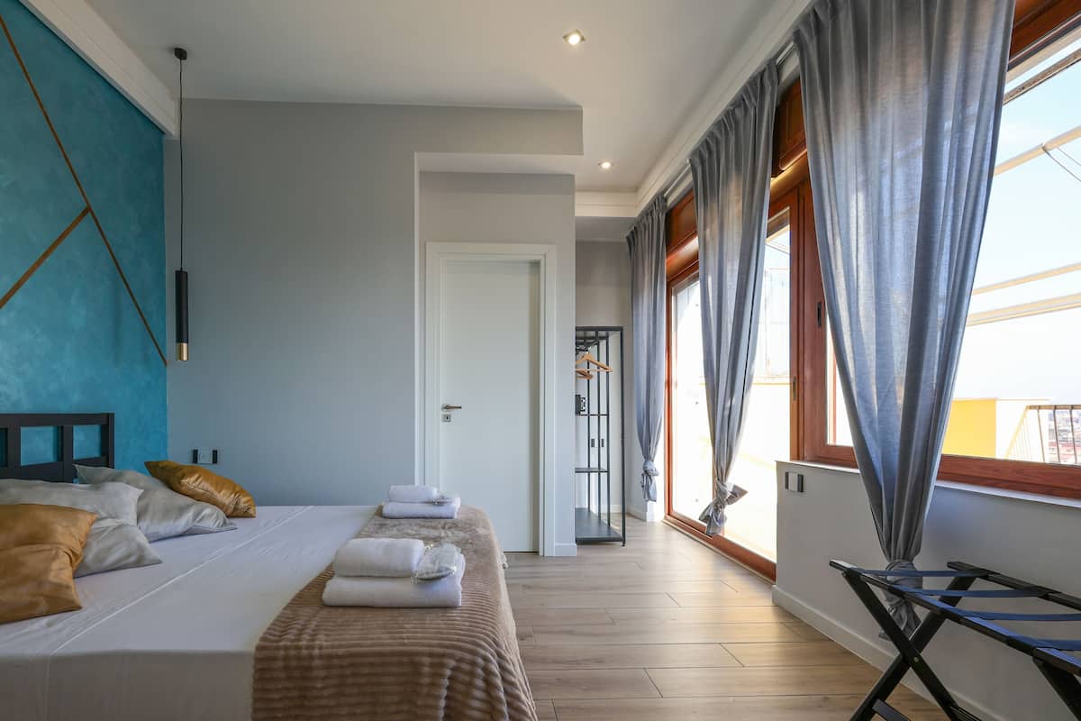 A hotel room with a large bed, a wardrobe, a window with curtains, and a view of the city.