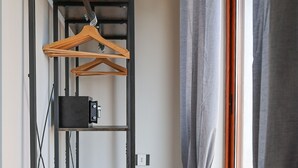 Um corredor com uma estante de metal, um cabide de madeira e uma janela com cortinas.