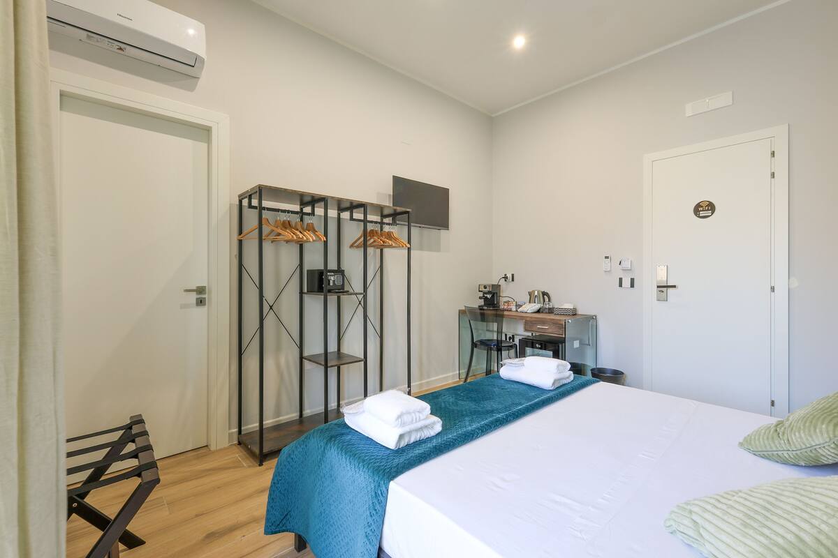 A hotel room with a bed, a desk, a wardrobe, and a bench.