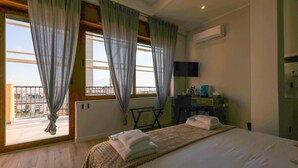 Quarto de hotel com cama, escrivaninha, cadeira, televisão e janela com cortinas.