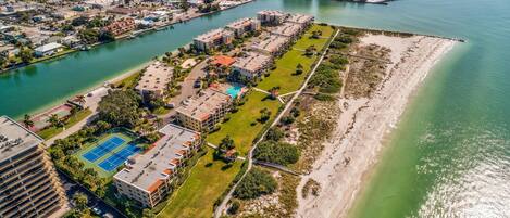 An aerial view of a coastal residential area with a marina, a tennis court, and a beach.