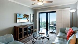 A living room with a glass coffee table, leather sofa, and a ceiling fan. - Land's End 10-302 Beach Front - Premier (Treasure Island)
