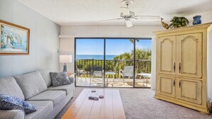 A living room with a sofa, coffee table, and a cabinet. There is a balcony with a view of the ocean. - Land's End 10-305 Beach Front (Treasure Island)