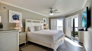 Une chambre à coucher avec un lit, des tables de chevet, un ventilateur de plafond, une télévision et une vue sur l’extérieur.