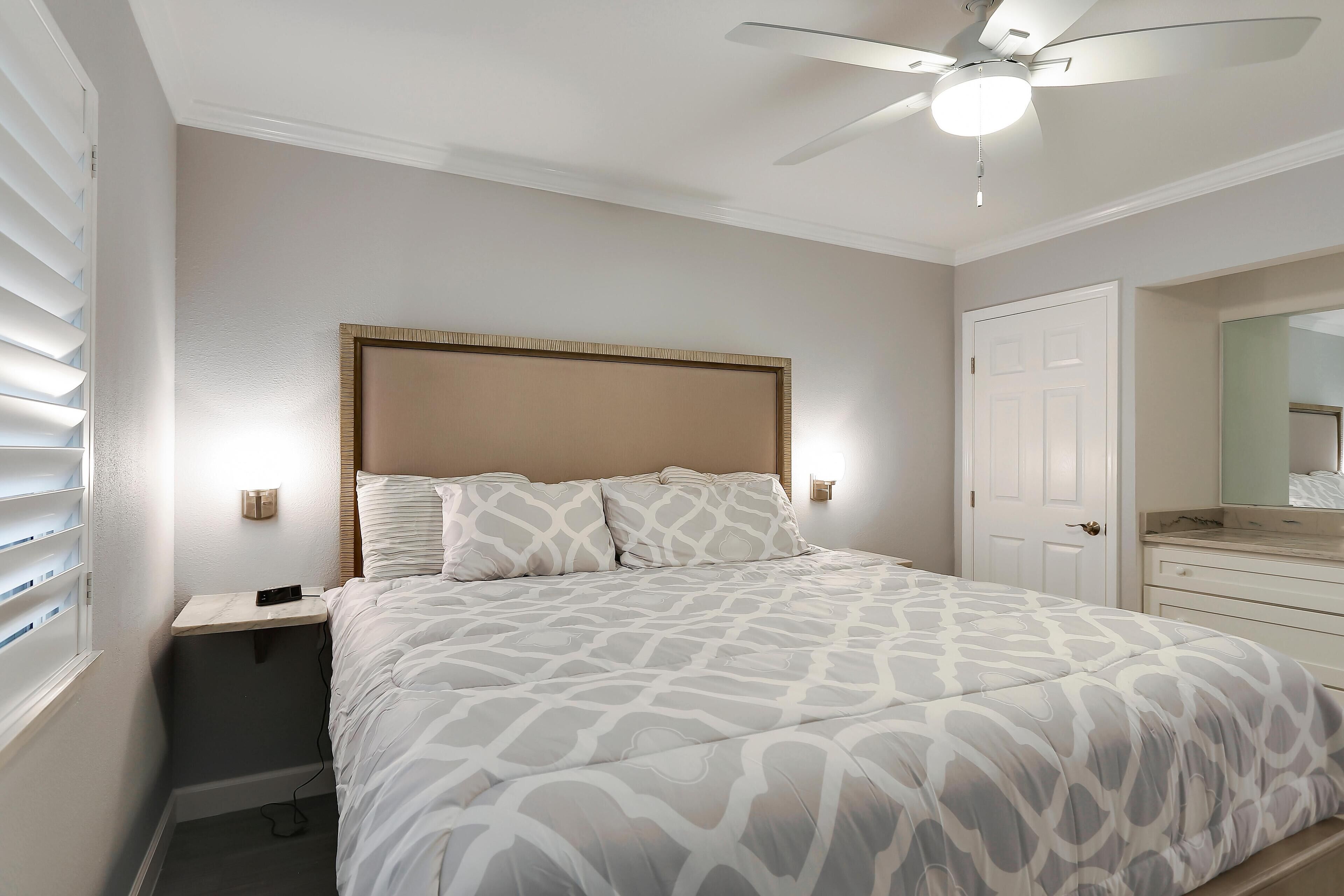 A bedroom with a bed, bedside tables, a ceiling fan, and a door.