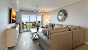 Uma sala de estar moderna com um sofá, uma mesa de centro e uma TV. Há uma varanda com vista.
