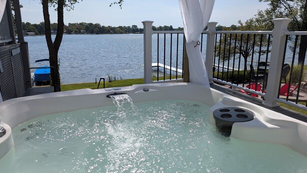 Un bain à remous avec vue sur un lac, entouré d’une balustrade blanche et d’arbres.