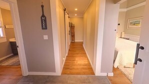 Un couloir doté d’un plancher en bois, de murs de couleur beige et d’une porte ornée d’un rideau blanc.
